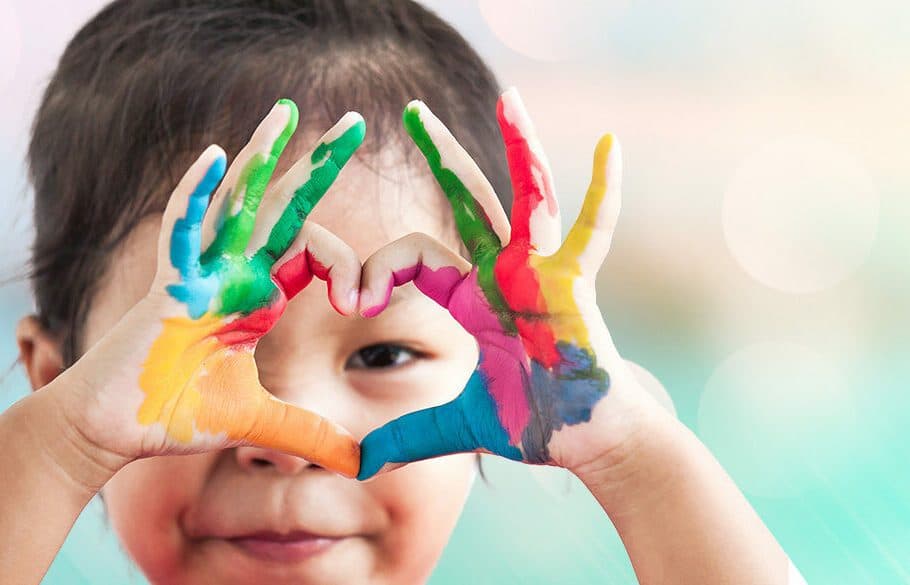 A child making a heart shape with painted hands at The Village Learning Center